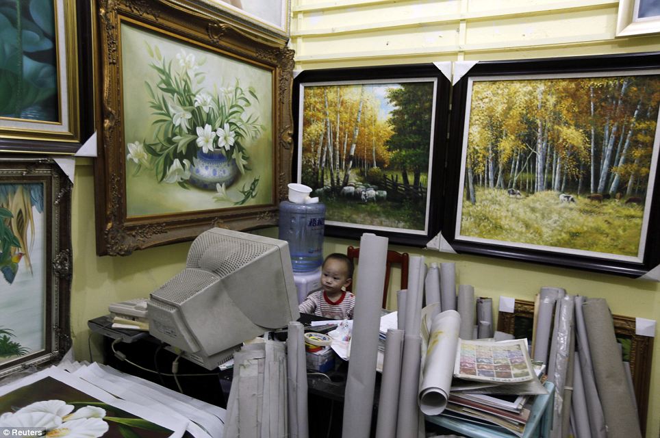 Start them young: A two-year-old boy, the son of a vendor, sits watching cartoons on an old computer surrounded by dozens of rolled up and hanging canvases at a gallery at Dafen